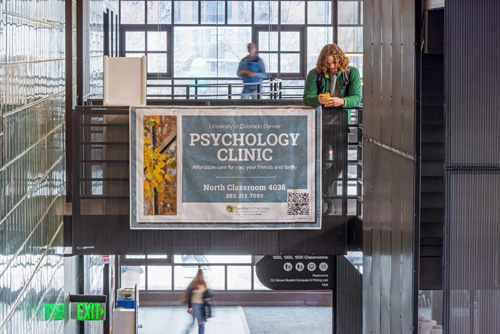 A photo of a banner advertising the CU Denver Psychology Clinic hangs in a light-filled building atrium
