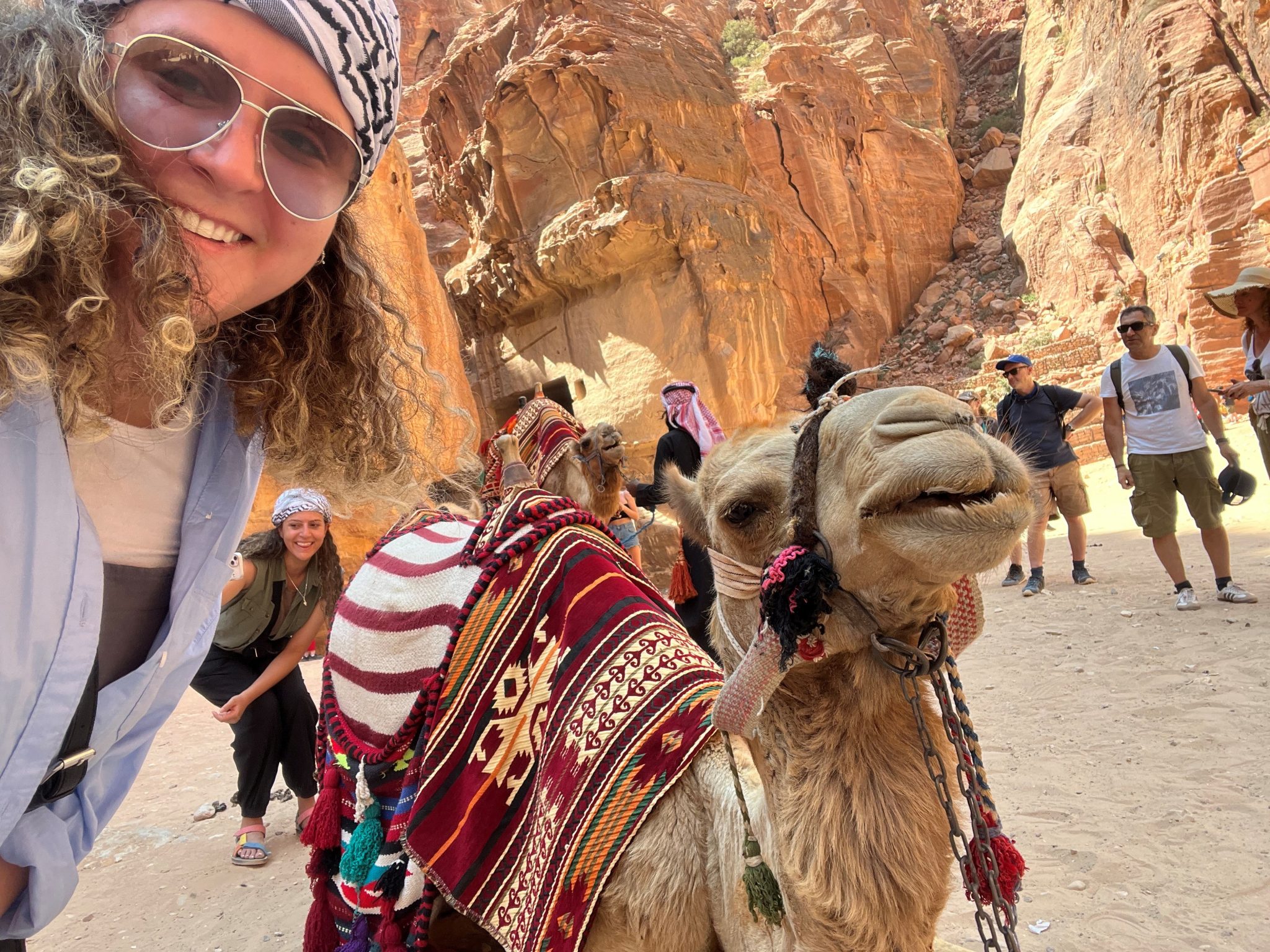 A photo of Sara Khammash wearing sunglasses and posing with a camel in a desert setting
