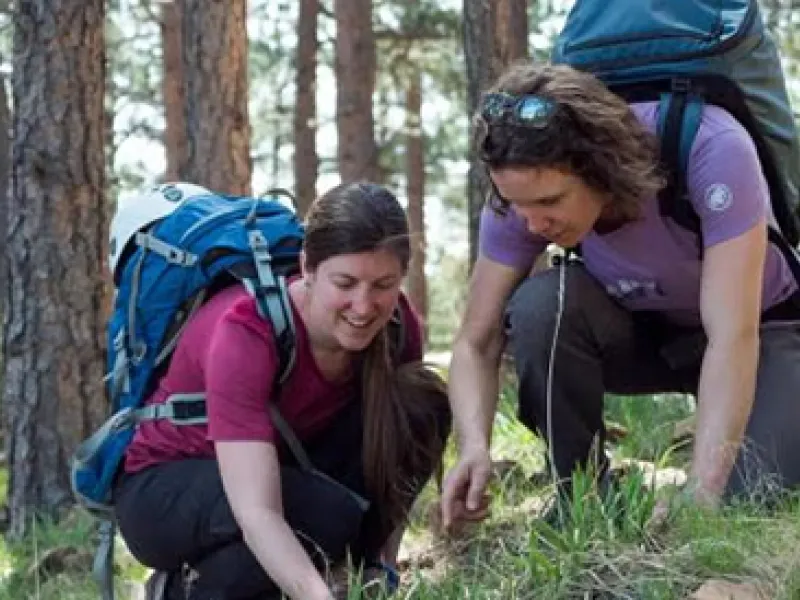 Two students wearing blue backpacks in a forest