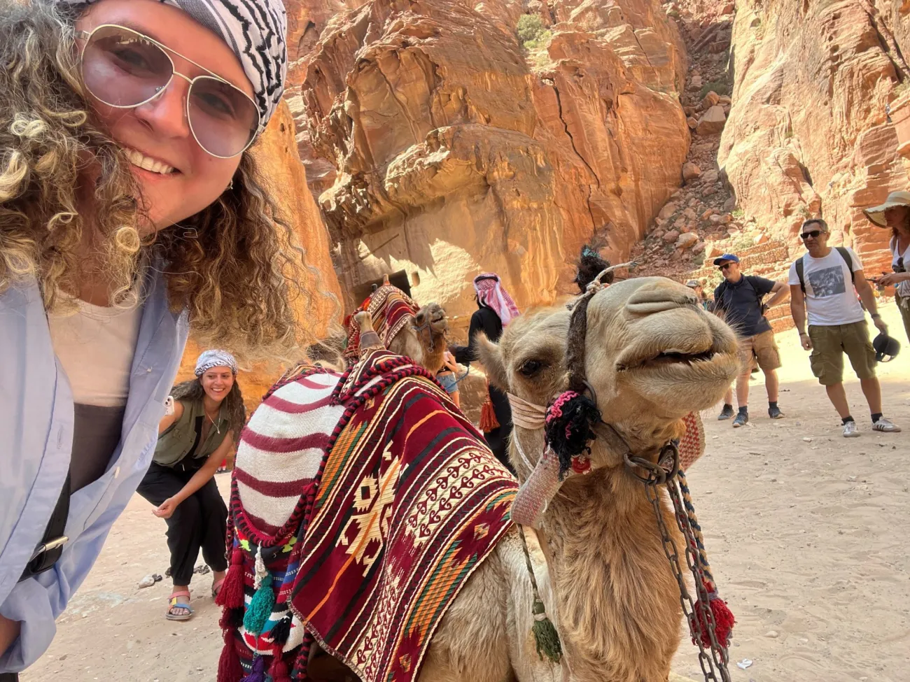 A photo of Sara Khammash wearing sunglasses and posing with a camel in a desert setting